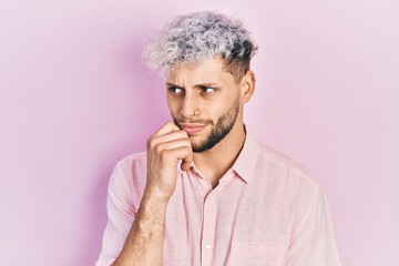 Young hispanic man with modern dyed hair wearing casual pink shirt thinking concentrated about doubt with finger on chin and looking up wondering