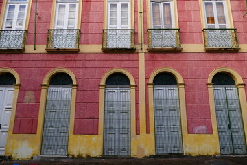 Parts of an old house facade in old pink and orange yellow, with windows and decorative wrought iron window grilles from around 1900, colonial style in the tropical metropolis of Manaus, Brazil.
