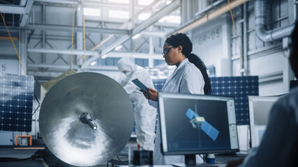 Female Engineer Uses Tablet Computer while Working on Satellite Construction. Aerospace Agency Manufacturing Facility: Scientists Build, Assemble Spacecraft for Space Exploration, Observation Mission