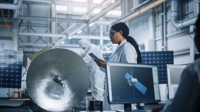Female Engineer Uses Tablet Computer while Working on Satellite Construction. Aerospace Agency Manufacturing Facility: Scientists Build, Assemble Spacecraft for Space Exploration, Observation Mission