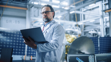 Male Engineer Confident and Focused Thinking, working on Laptop at Aerospace Satellite...