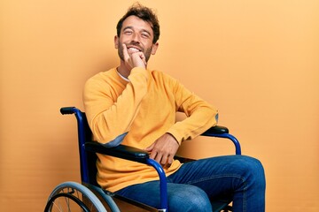 Handsome man with beard sitting on wheelchair looking confident at the camera smiling with crossed arms and hand raised on chin. thinking positive.