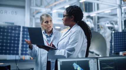 Two Female Engineers Talk, Use Computer working at Aerospace Satellite Manufacturing Facility....