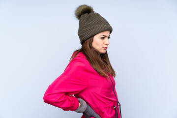 Young girl with winter hat isolated on blue background suffering from backache for having made an effort