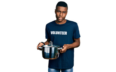 Young african american man wearing volunteer holding cooking pot clueless and confused expression. doubt concept.