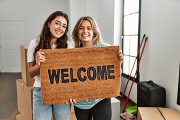 Young beautiful couple smiling happy holding welcome doormat at new home.