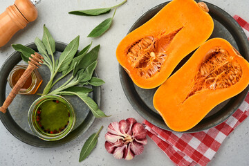 Halves of raw organic butternut squash with sage leaf, multicolored pepper garlic, honey, salt and pepper on a white slate, stone or concrete background. Food background. Top view with copy space.