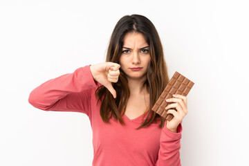 Fototapeta premium Young caucasian woman isolated on pink background taking a chocolate tablet making bad signal