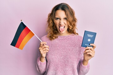 Young caucasian woman holding germany flag and passport sticking tongue out happy with funny...