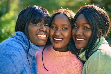 Three african american friends smiling happy hugging at the park.