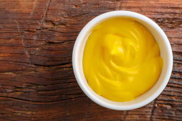 White gravy boats with cheese sauce on a wooden table.