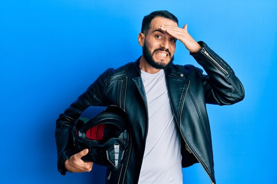 Young man with beard holding motorcycle helmet stressed and frustrated with hand on head, surprised and angry face