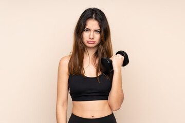 Young sport woman making weightlifting isolated on beige background sad