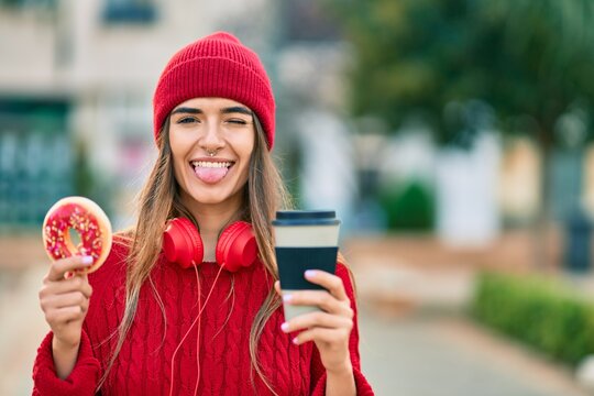 Young hispanic woman having breakfast using headphones at the city.