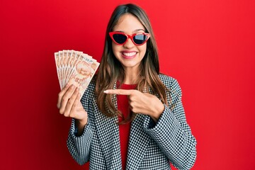 Young brunette woman holding 50 turkish lira banknotes smiling happy pointing with hand and finger - obrazy, fototapety, plakaty