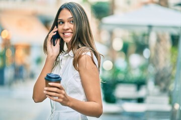 Beautiful latin teenager girl talking on the smartphone and drinking coffee at the city.