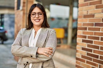 Young hispanic businesswoman smiling happy with arms crossed gesture at the city.