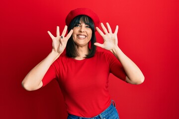 Young hispanic woman wearing french look with beret showing and pointing up with fingers number...