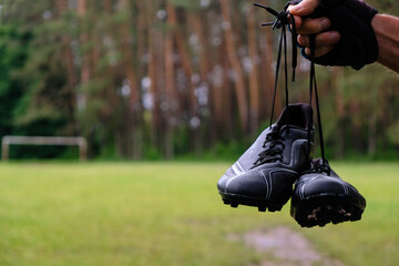 Black football boots in men's hands on a football field background. Raindrops on shoes. Forest...