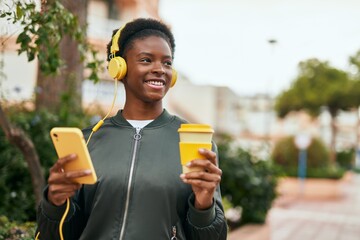Fototapeta premium Young african american girl drinking coffee using smartphone and headphones at the city