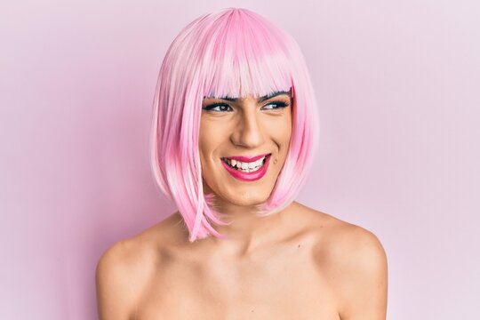 Young man wearing woman make up wearing pink wig looking away to side with smile on face, natural expression. laughing confident.