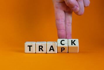 Trap or track symbol. Businessman turns wooden cubes and changes the word 'trap' to 'track'. Beautiful orange table, orange background, copy space. Business, trap or track concept.