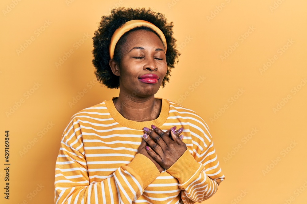 Wall mural Young african american woman wearing casual sweatshirt smiling with hands on chest, eyes closed with grateful gesture on face. health concept.