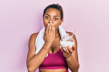 Young african american girl wearing sportswear holding sugar covering mouth with hand, shocked and...