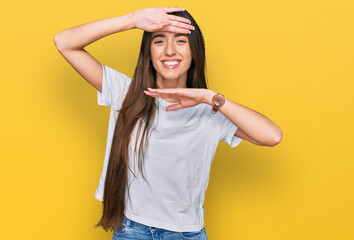 Young hispanic girl wearing casual white t shirt smiling cheerful playing peek a boo with hands showing face. surprised and exited