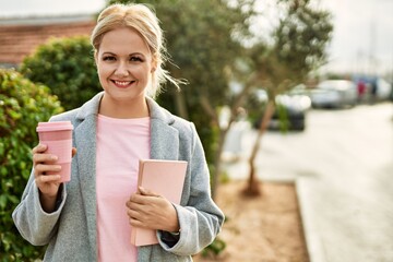 Young blonde businesswoman smiling happy drinking coffee at the city.