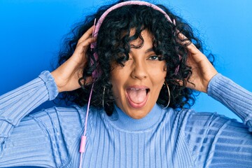 Young hispanic woman listening to music using headphones winking looking at the camera with sexy...