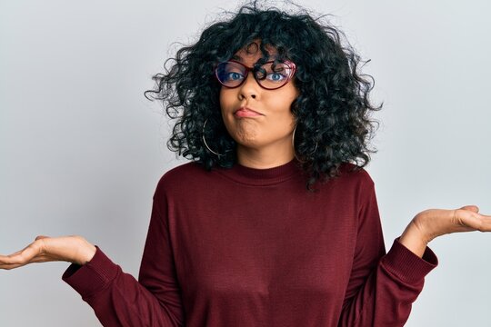 Young hispanic woman wearing casual clothes and glasses clueless and confused with open arms, no idea and doubtful face.