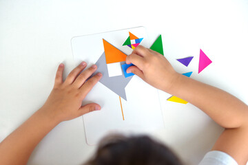 A preschooler girl sitting at the table collects a drawing from a geometric figure. the concept of early childhood development by montessori. a game of logic and imagination.