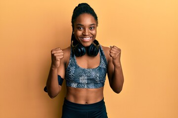 African american woman with braided hair wearing sportswear and arm band celebrating surprised and amazed for success with arms raised and open eyes. winner concept.