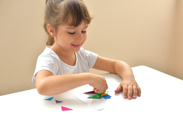 A preschooler girl sitting at the table collects a drawing from a geometric figure. the concept of...