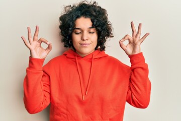 Young hispanic woman with curly hair wearing casual sweatshirt relax and smiling with eyes closed doing meditation gesture with fingers. yoga concept.