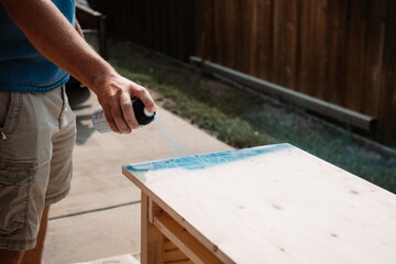 Hand of young man paints an unfinished table with blue spray paint