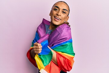 Hispanic man wearing make up and long hair wrapped in rainbow lgbtq flag celebrating crazy and...