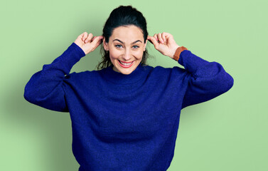 Young hispanic woman wearing casual clothes smiling pulling ears with fingers, funny gesture....