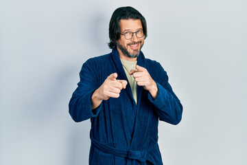 Middle age caucasian man wearing bathrobe and glasses pointing fingers to camera with happy and funny face. good energy and vibes.