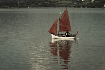 Traditional style red sails on small yacht becalmed in bay.