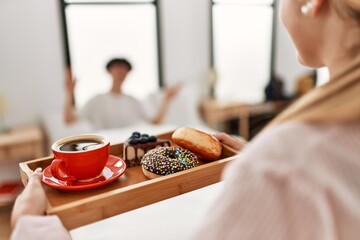 Woman surprising her boyfriend with breakfast on the bed at home.