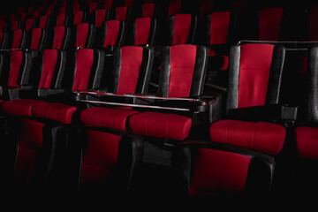 Empty movie theater. Armchairs red and black in the cinema hall are illuminated by a beam of light, low key. Selective focus. Quarantine, restrictive tape on chairs