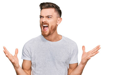 Naklejka premium Young redhead man wearing casual grey t shirt crazy and mad shouting and yelling with aggressive expression and arms raised. frustration concept.