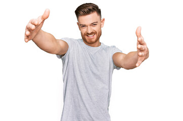 Fototapeta premium Young redhead man wearing casual grey t shirt looking at the camera smiling with open arms for hug. cheerful expression embracing happiness.