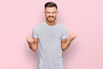 Young redhead man wearing casual grey t shirt excited for success with arms raised and eyes closed celebrating victory smiling. winner concept.