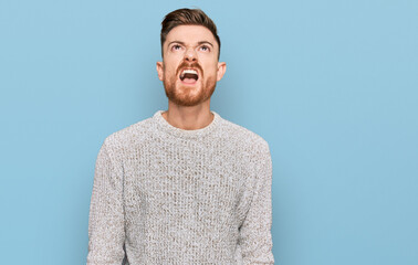 Young redhead man wearing casual winter sweater angry and mad screaming frustrated and furious, shouting with anger. rage and aggressive concept.