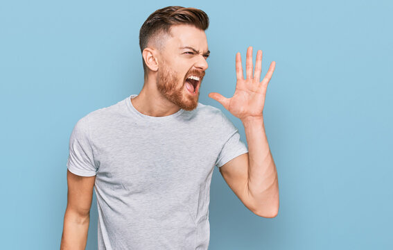 Young redhead man wearing casual grey t shirt shouting and screaming loud to side with hand on mouth. communication concept.
