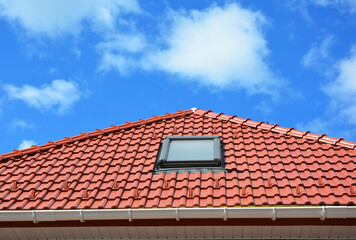 Roofing construction. A red metal roof with a attic skylight window installed, a plastic rain...