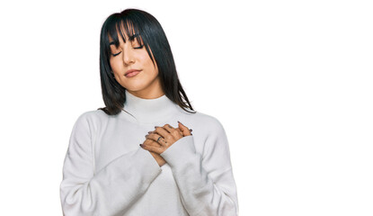 Young brunette woman with bangs wearing casual turtleneck sweater smiling with hands on chest with...